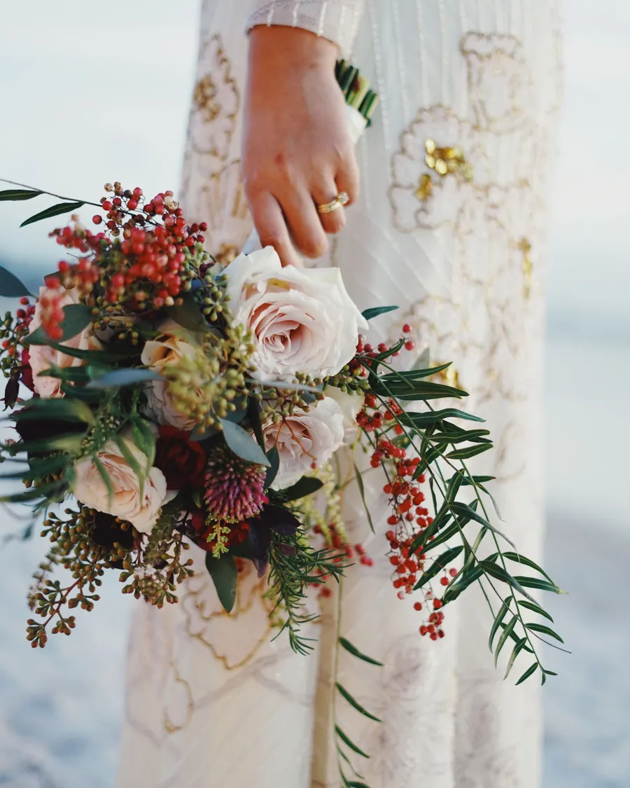 Bride in a lace dress holding a trailing bouquet with berries